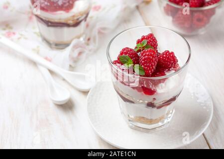 Käsekuchen mit Himbeeren in Brille auf weißem Holzhintergrund Stockfoto