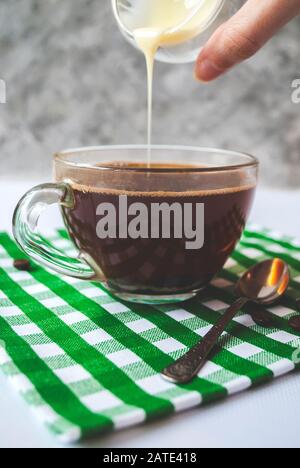 Transparente Tasse Kaffee mit gießenden Kondensmilch Stockfoto