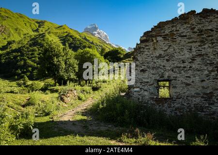 Ruinen eines alten georgischen Hirtenhäuschens auf dem Weg zum Guli-Pass in den Kaukasusbergen mit dem Gipfel des Ushba im Hintergrund. Stockfoto