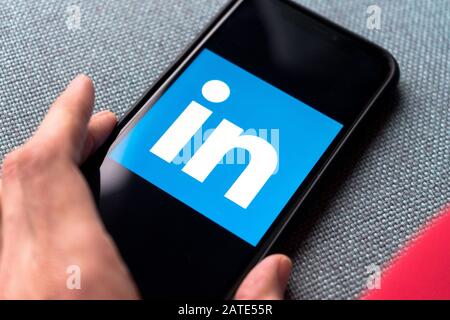 Junge Frau hält ein Smartphone mit Linkedin-App auf dem Bildschirm. IPhone 11 mit einem Logo für Social Media Professional und Job Interview App. Stockfoto