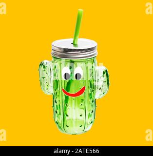 Glasgrüne transparente Flasche mit Metallkappe und Strohhalm in Form eines Kakteens und einer niedlichen Schnauze auf gelbem Hintergrund. Sommergetränk auf einer Brigh Stockfoto