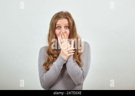 Schöne rothaarige Frau im grauen Pullover mit überraschtem Ausdruck zeigt Schock Stockfoto