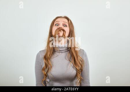 Die rothaarige Frau im grauen Pullover machte ihr Haar zur Nachahmung des Schnurrbarts des Mannes Stockfoto