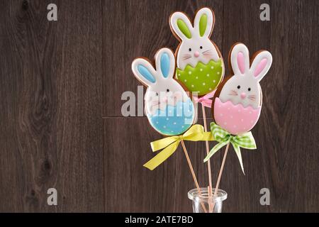 Vorderansicht der Ingwerplätzchen in Vase isoliert auf Holzhintergrund. Hausgemachtes, köstliches Gebäck in Form von osterhasen mit bunten Eiern auf Holzstäbchen. Konzept der Feiertage. Stockfoto