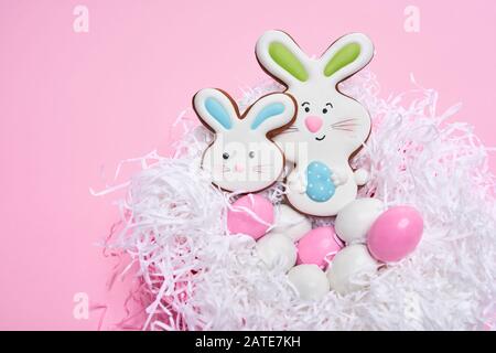 Von oben Blick auf glasierte Plätzchen in Form von hübschen Hasen und bunten Eiern, die in weißem Gelege liegen, isoliert auf pinkfarbenem Hintergrund. Nahaufnahme von süßem Gebäck. Frühlings- und osterfeiertage Konzept. Stockfoto