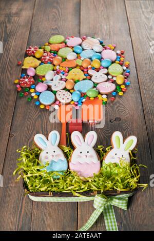 Bunte Ingwer glasierte Plätzchen auf Tisch und in Box mit Gras, Schokoladenkugeln mit Zuckerschale und Silikonspatel. Hausgemachtes, schönes Gebäck aus ostertieren, Eiern und Karotten in Kreisform. Stockfoto