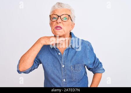 Eine Frau mit einem Denimhemd und einer Brille über einem isolierten weißen Hintergrund, die mit der Hand als Messer die Kehle durchschneidet, bedroht Aggressionen mit Fu Stockfoto