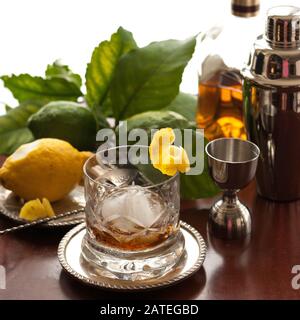 Ein Kristallglas Whisky mit einem großen, kugelförmigen Eisstück und Zitruspergarnierung. Stockfoto