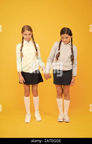 Gefühl schüchtern. Süße Kinder, Hände auf gelben Hintergrund. Kleine Kinder tragen Schuluniform. Schule Kinder mit Mode schauen. Kleine Kinder mit geflochtenem Haar sind zurück in die Schule. Stockfoto