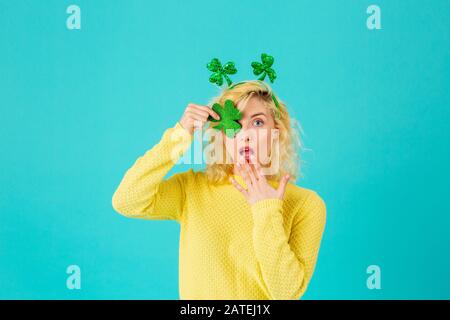 Studio-Porträt einer jungen Frau, die Shamrock hält, eine Eie mit offenem Mund bedeckt, überrascht, mit St. Patrick's Day Kopfschmuck Stockfoto