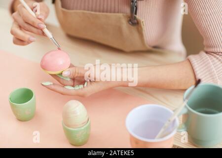 Nahaufnahme einer nicht erkennbaren Frau, die für Ostern Eier in Pastellfarben malt, während sie in Küche oder Kunststudio am Tisch sitzt, Kopierraum Stockfoto