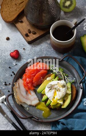 Valentinstag Frühstück. Gekochtes Eier-Sandwich mit Avocado, Kaffee, Lachs und geräuchertem Lachs auf einer Tischplatte aus Steinbeton. Stockfoto