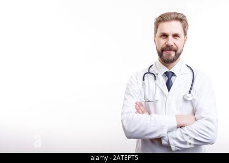 Lächelnder bärtiger Arzt in weißem Mantel mit Stethoskop, das Arme aufwirft, die isoliert weißen Hintergrund Copyspace Stockfoto