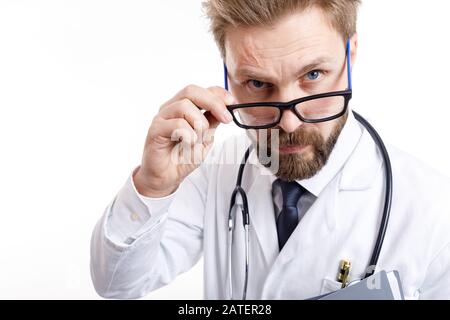 Nahaufnahme des jungen bärtigen Arztes mit Stethoskop, das die Kamera über eine Brille blickt, isolierter weißer Hintergrund Stockfoto