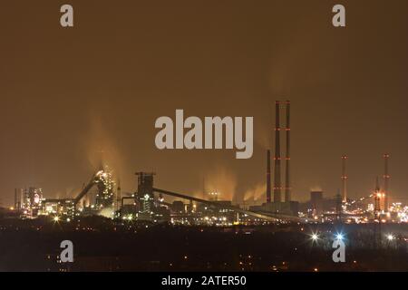 Eine dunkle und schmutzig aussehende Stahl- und Kokerei in der Ferne bei Nacht. Stockfoto