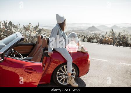 Lifestyle-Porträt einer stilvoll gekleideten Frau beiläufig in Jeans und Hut sitzend auf dem Auto, genießen Sie die Fahrt auf der Insel Stockfoto