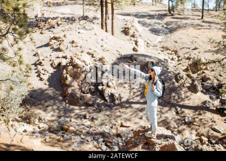 Stilvolle Frau, die schöne Landschaften auf vulkanischen Felsen im Kiefernwald genießt und hoch in den Bergen auf der Insel Tenera, Spanien, unterwegs ist Stockfoto