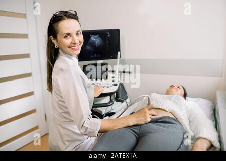 Junge lächelnde Frau Arzt Sonograph mit Ultraschallgerät während der Durchführung von Ultraschalltests des weiblichen Patienten Abdomen im Krankenhaus. Stockfoto