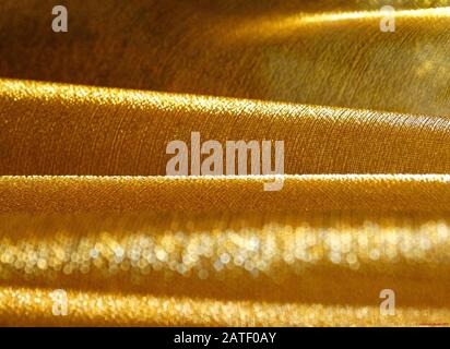 Voller Rahmen aus gefaltetem goldenem Stoff als Wellen aus goldenem hellem Bokeh Stockfoto