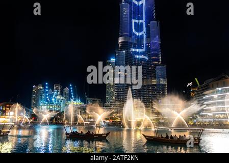 Touristenboote, die nachts die choreographierte Brunnenanzeige in Dubai la Fontane beobachten, spiegelten sich auf dem Wasser im Burj Khalifa Lake wider Stockfoto