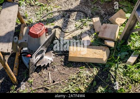 Eine elektrische manuelle Kreissäge liegt auf dem Boden in der Nähe von Holzbohlen, die nicht den Sicherheitsvorschriften entsprechen Stockfoto
