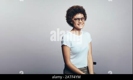 Porträt einer lächelnden jungen Frau, die Brillen trägt, die auf grauem Hintergrund isoliert sind. Lächelnde Geschäftsfrau mit lockigen Haaren und Blick auf die Kamera. Stockfoto