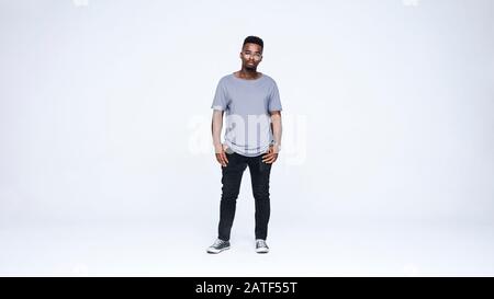 Junger afroamerikanischer Mann, der isoliert auf weißem Hintergrund steht. Junger Mann in Brille und legeren Kleidungsstücken mit Blick auf die Kamera. Stockfoto