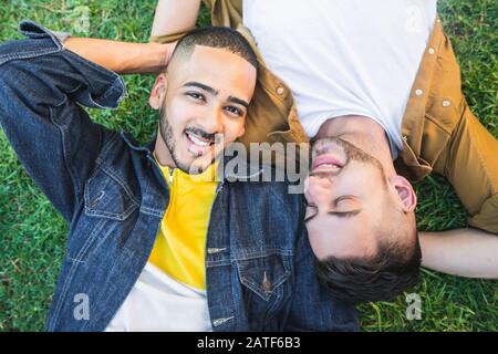 Porträt des jungen schwulen Paares, das schöne Zeit verbringt und sich auf dem Gras am Park niederlegt. LGBT und Love Konzept. Stockfoto