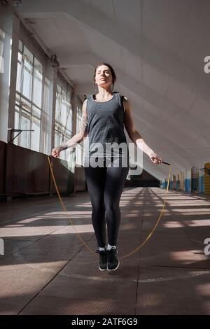 Junge, athletische Kaukasianerin im schwarzen Sportbekleidungsspringen mit Springseil Stockfoto