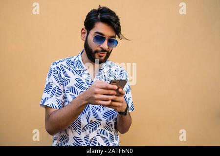 Porträt der jungen Latin mit seinem Handy vor gelbem Hintergrund Mann. Kommunikationskonzept. Stockfoto