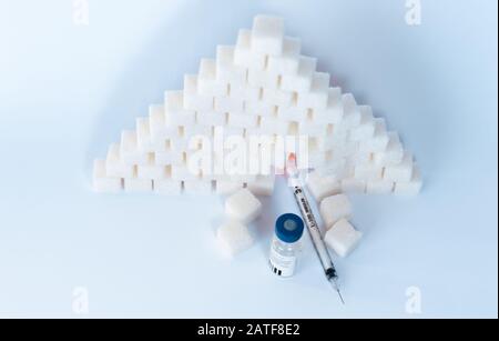 Zuckersucht, Insulinresistenz, ungesunde Ernährung, Zuckerwürfelpyramide, Insulinflaschen und Spritze zur Impfung auf weißem Hintergrund, Diabetes Stockfoto