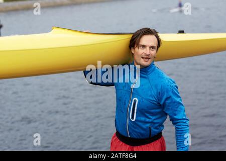 Mann mittleren Alters in Sportswear, der nach dem Paddeln ein kleines gelbes Boot trägt Stockfoto