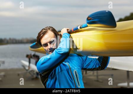 Junger kaukasischer blondenhaariger Mann mit gelbem Kajak Stockfoto