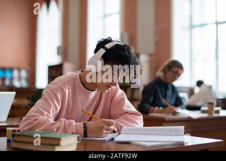 Cleverer Kerl in Casualwear, der Informationen aus dem Buch in seinem Copybook umschreibt Stockfoto