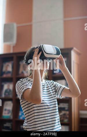 Modernes Teenager-Mädchen mit vr-Headset, das 3D-Filme in der Bibliothek sieht Stockfoto