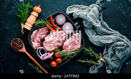 Rohsteak. Fleisch mit Gewürzen und Kräutern. Auf schwarzem Steingrund. Draufsicht. Freier Speicherplatz. Stockfoto