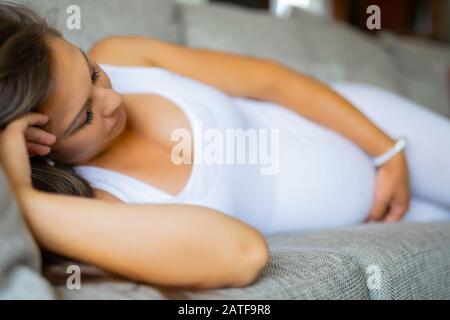 Ängstliche schwangere Frau, die mit Schmerzen auf dem Sofa liegt Stockfoto