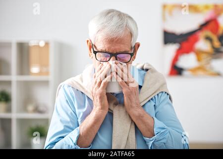 Kranker älterer pensionierter Mann mit Taschentuch an der Nase, der zu Hause bleibt Stockfoto