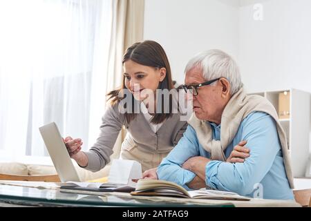 Junge Brunette-Frau, die ihrem älteren Vater zeigt, wie man online einkaufen kann Stockfoto