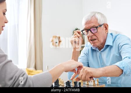Der Senior deaktiviert den Mann in Brillen und Hemden, die Schach mit Sozialarbeitern spielen Stockfoto