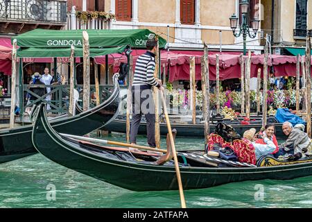 Touristen, die eine Gondelfahrt genießen, während der Gondelfahrer seine Gondel durch den geschäftigen Canal Grande in Venedig, Venedig, Italien lenkt Stockfoto