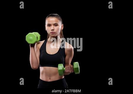 Hübsches Mädchen in schwarzem Aktivewear mit grünen Hanteln während des Trainings Stockfoto