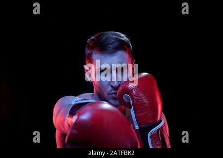 Junger Sportler in Boxhandschuhen trifft Rivale vor ihm beim Kampf Stockfoto