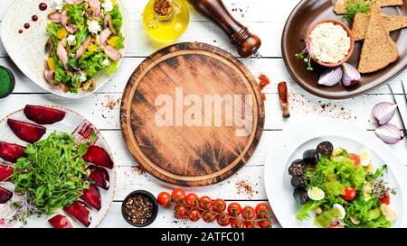 Essen. Salate und Gerichte auf weißem Holzhintergrund. Draufsicht. Freier Speicherplatz für Ihren Text. Rustikaler Stil. Stockfoto