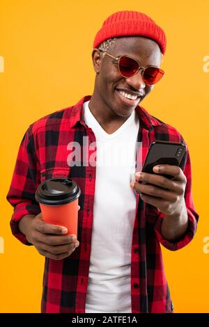 Porträt eines schwarzen amerikaners, der stilvoll ein Getränkeglas auf Kaffeepause mit hellgelbem Hintergrund hält. Stockfoto