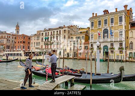 Zwei Gondoliers, die auf einem kleinen Steg stehen und ein Schild entlang des Canal Grande in Venedig, Italien, einstellen Stockfoto