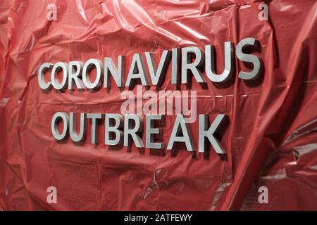 Die Worte Coronavirus Ausbruch gelegt mit silbernen Metallbuchstaben auf Zerknitterte rote Kunststofffolie Stockfoto