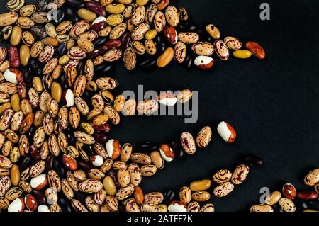 Verschiedene Bohnen auf dem Tisch verstreut. Natürliche Produkte auf dunklem Hintergrund. Stockfoto