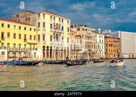 Gondeln und ein Wassertaxi auf Dem Canal Grande, während das Sonnenlicht am späten Nachmittag die Gebäude entlang des Canal Grande in Venedig, Italien, reflektiert Stockfoto