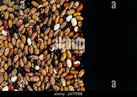 Verschiedene Bohnen auf dem Tisch verstreut. Natürliche Produkte auf dunklem Hintergrund. Stockfoto